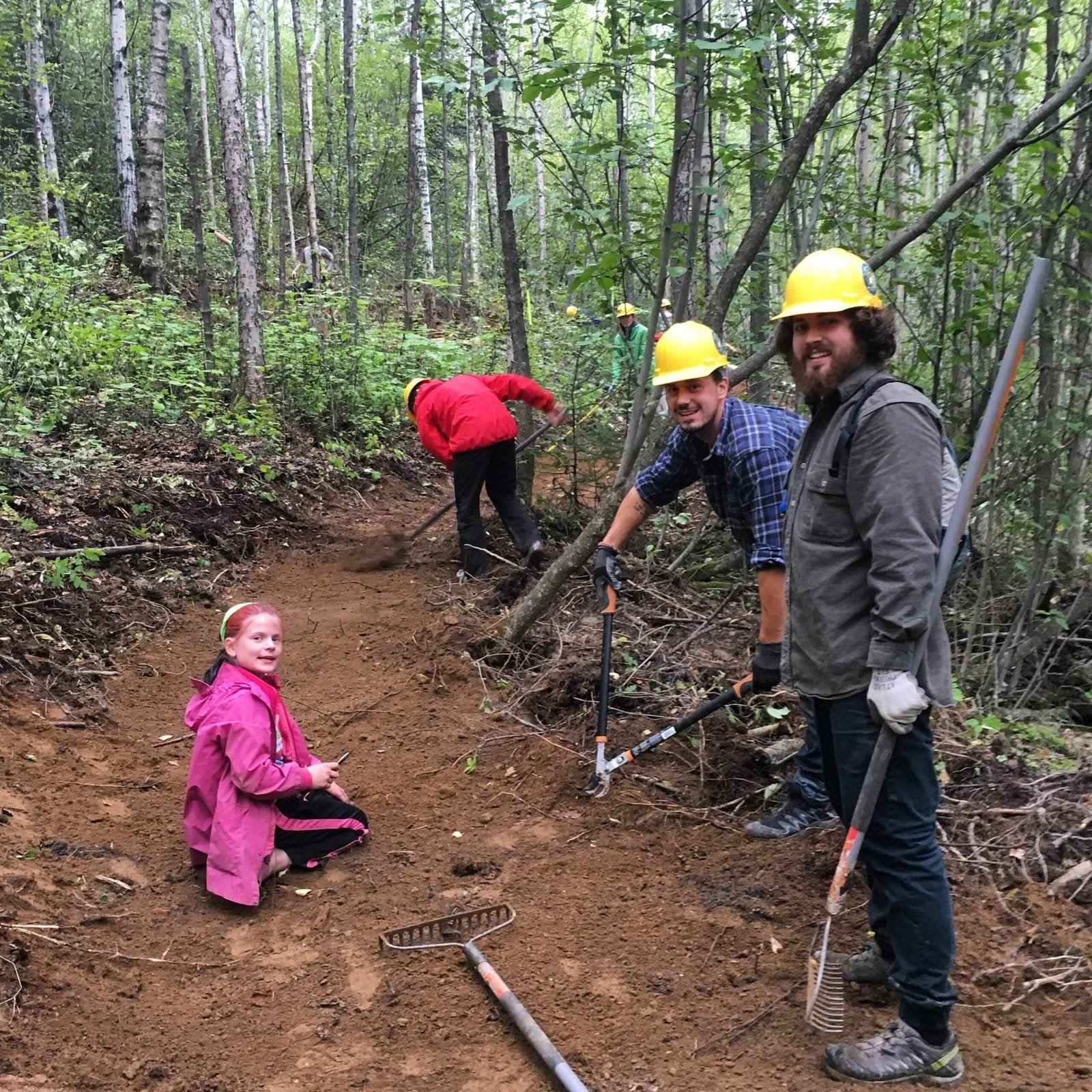 Volunteers with yellow helmets and a girl in a pink raincoat working on new mountain bike trails.