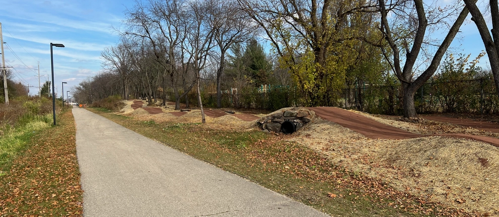 A dirt bike trail with rollers running beside a paved multi-use path